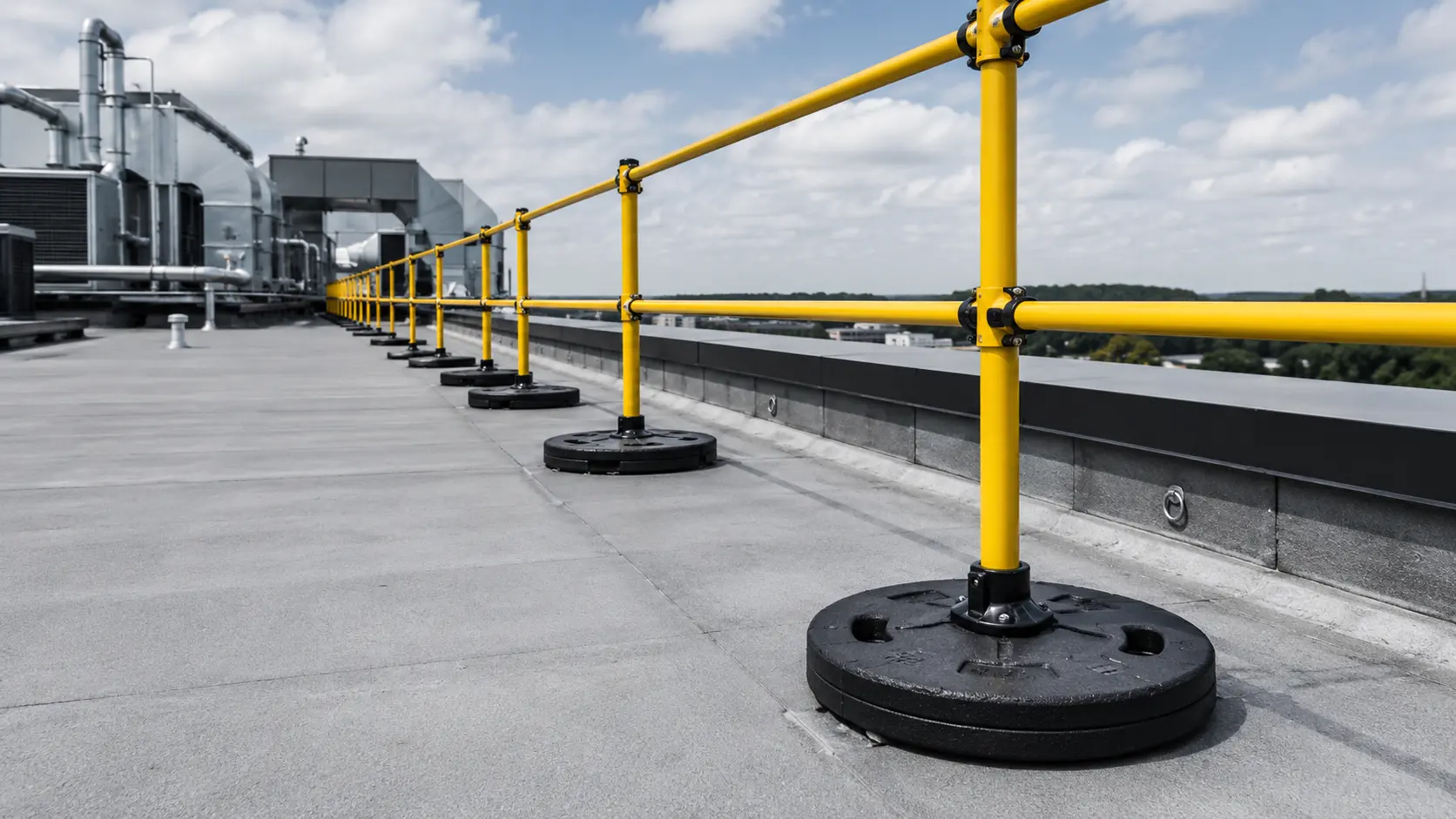 Industrial rooftop guardrail safety system with weighted freestanding railing bases on commercial building